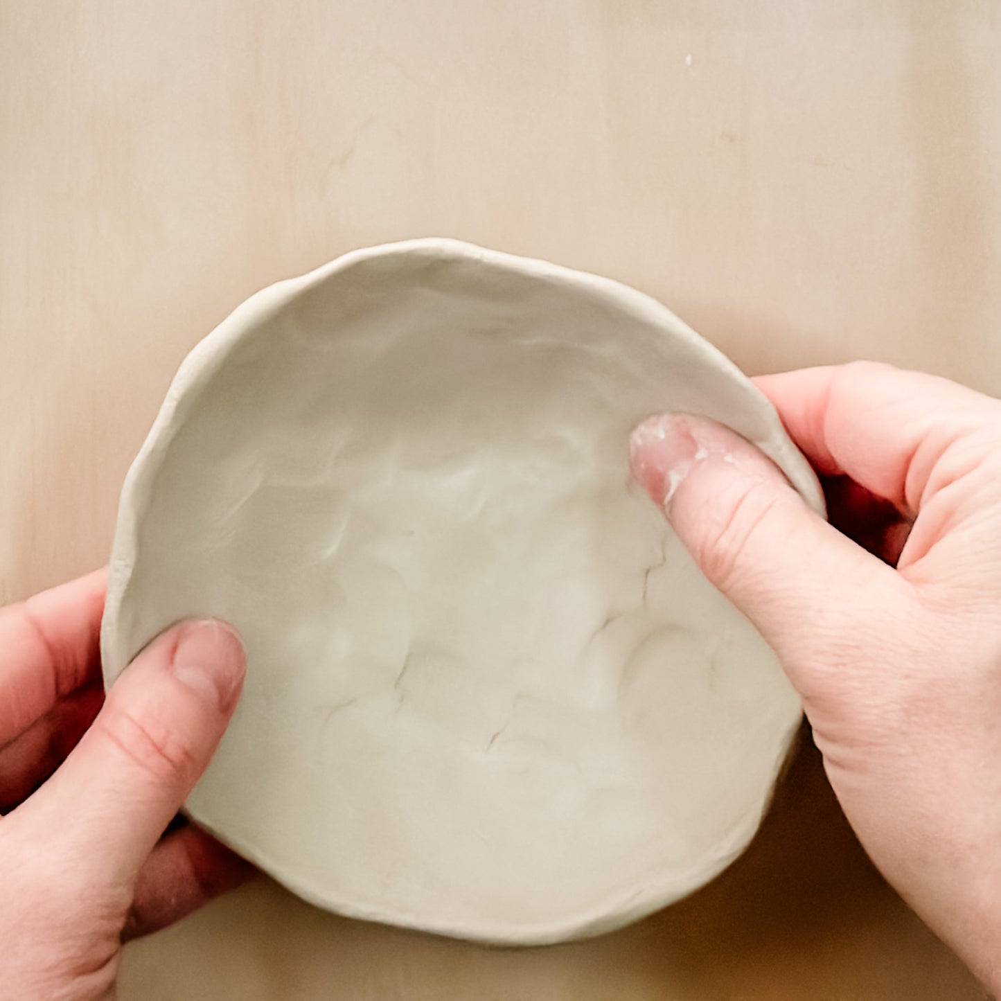 Person making a small ceramic bowl against a plain background