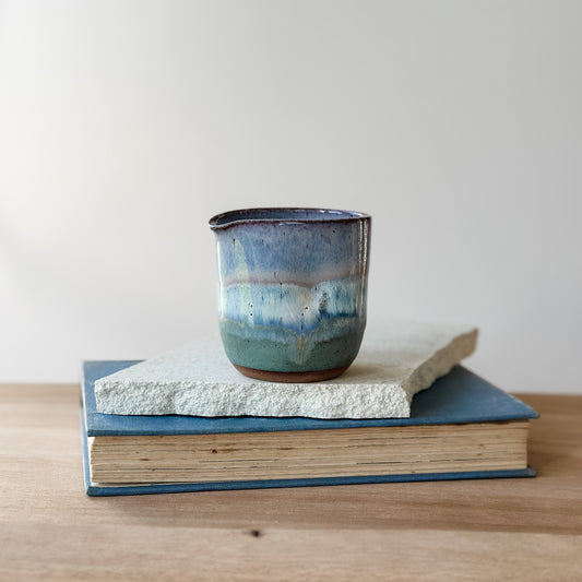 Ceramic creamer jug with blue glaze on a tile and a book against a plain background