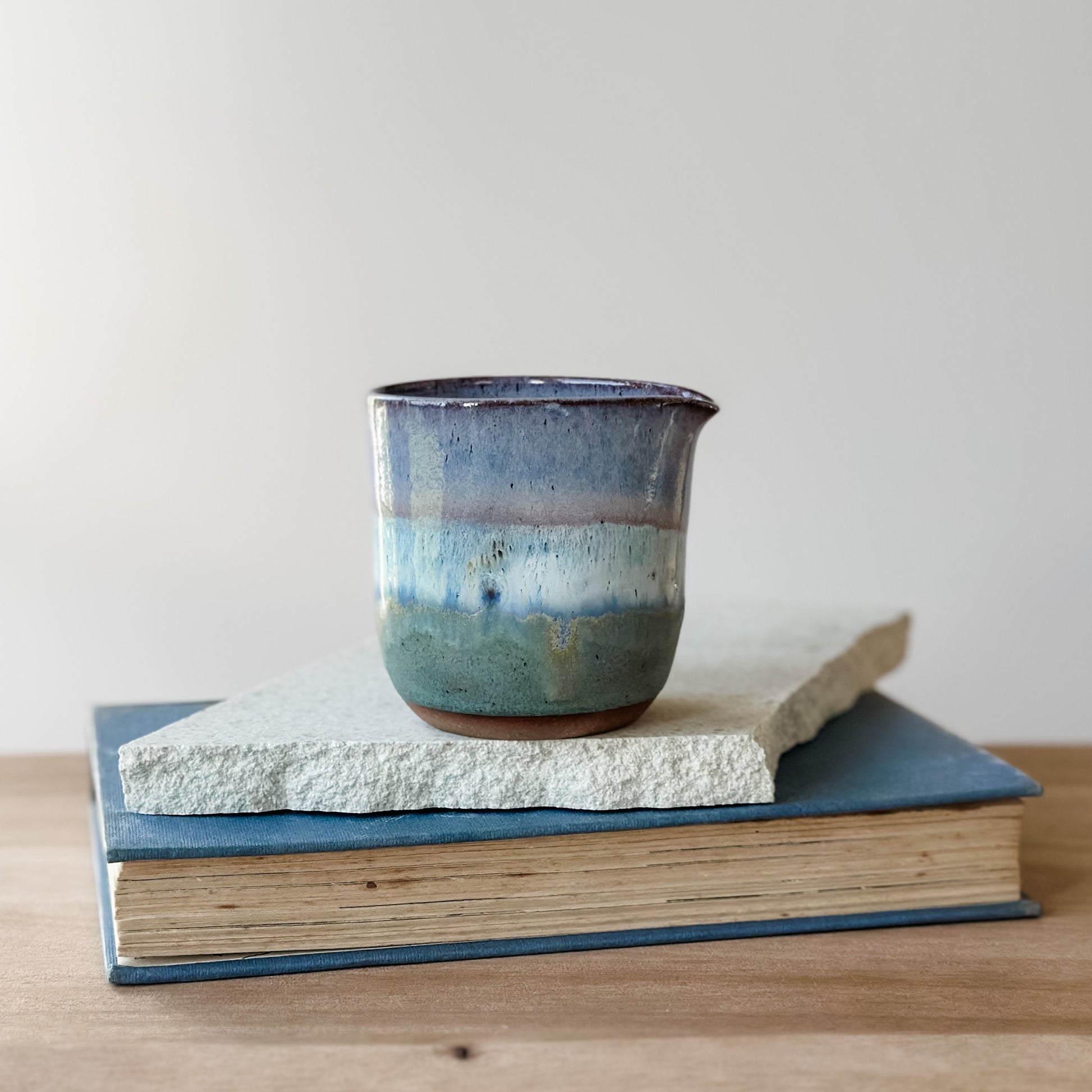 Ceramic creamer jug with blue and purple glaze on top of a book