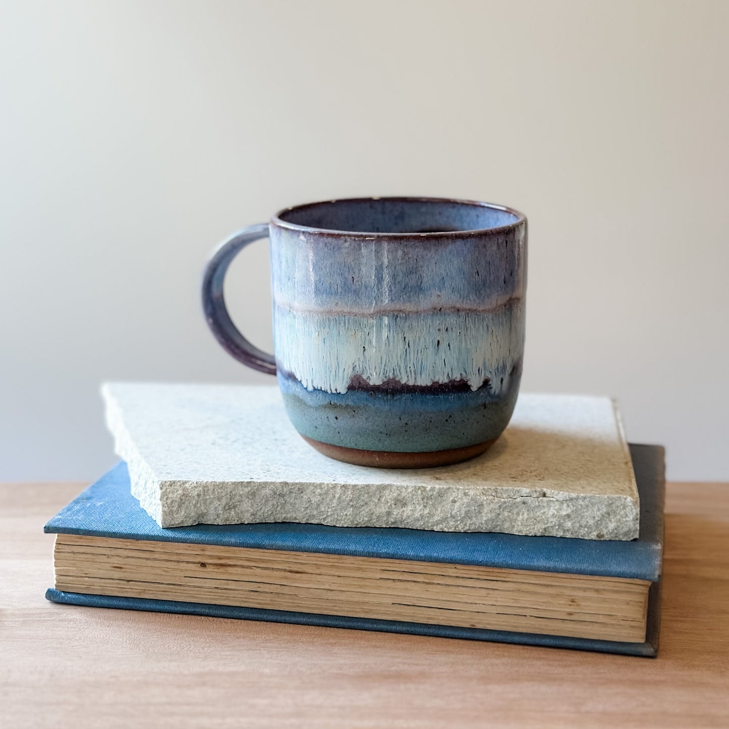 Ceramic mug with purple, white, and blue glaze on top of a book.