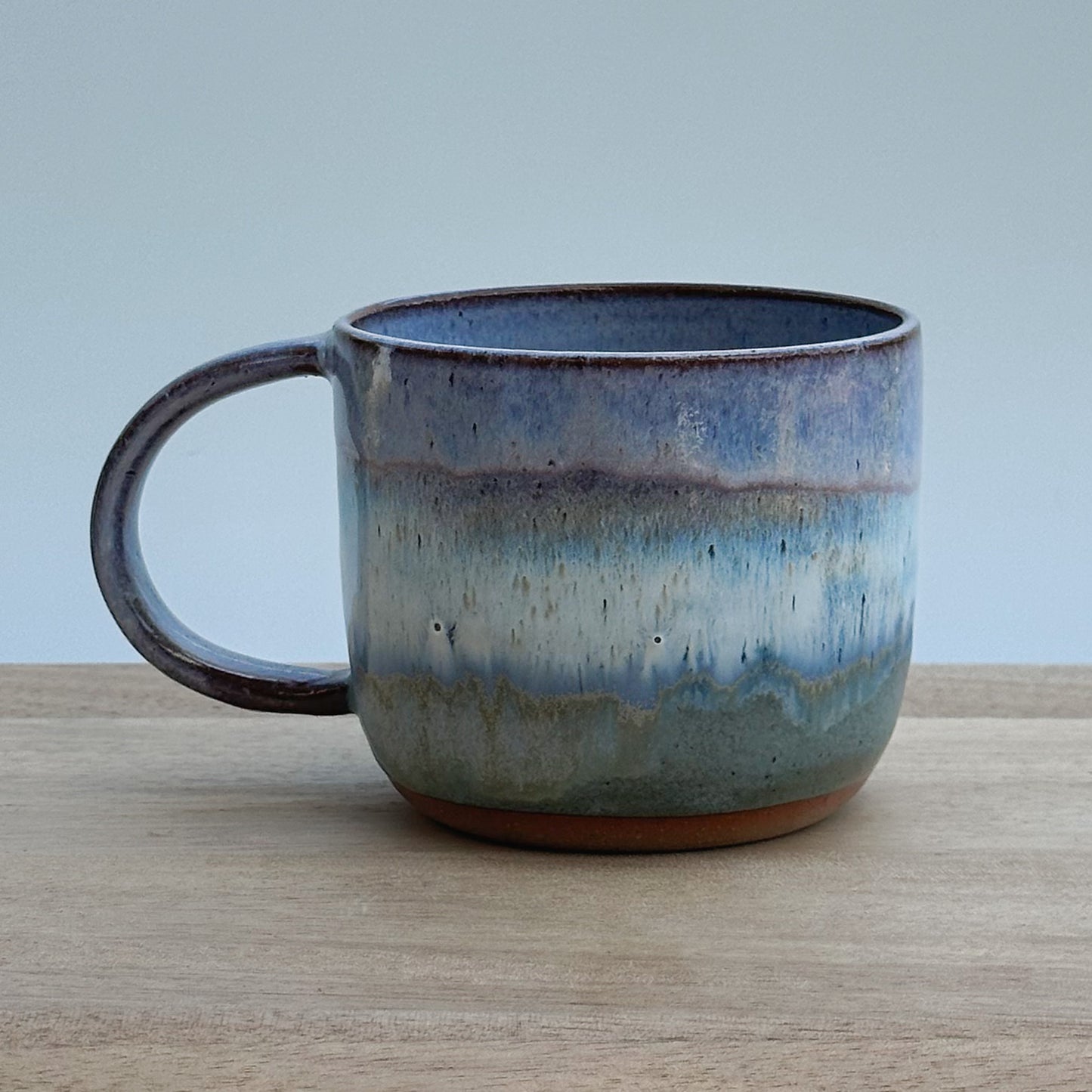 Ceramic mug with a purple, blue and brown glaze on a wooden surface