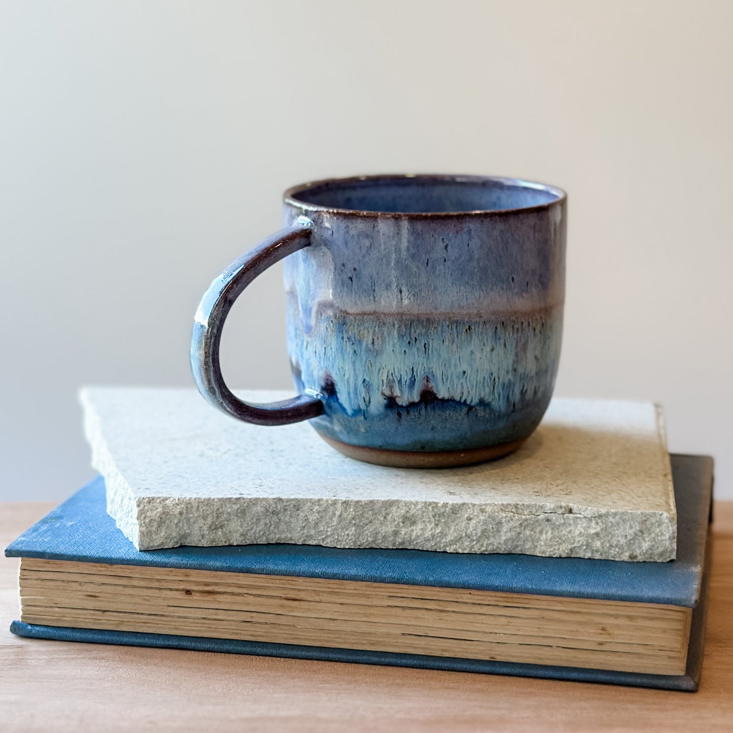 Blue ceramic mug on top of a tile and a book with a plain background