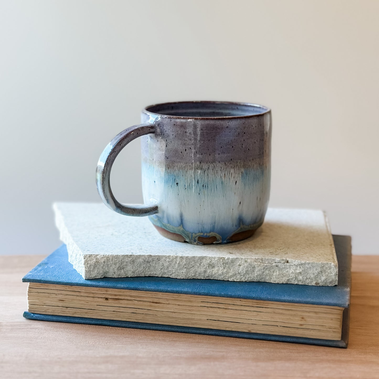 Ceramic mug on top of a stack of books with a plain background