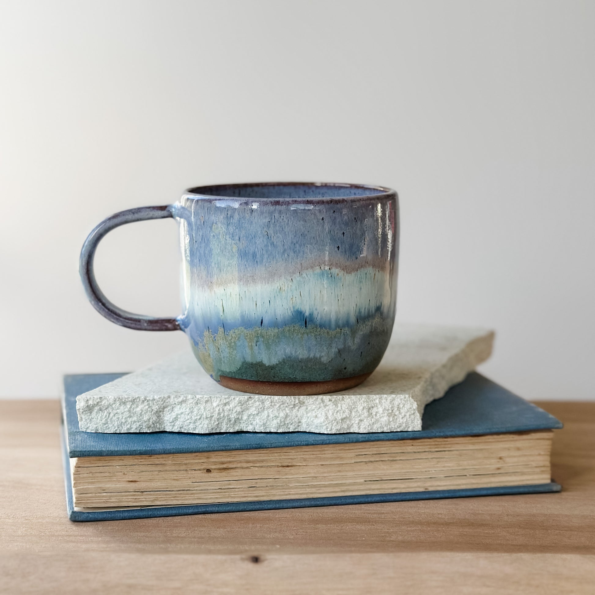 Blue ceramic mug on a stack of books with a plain background