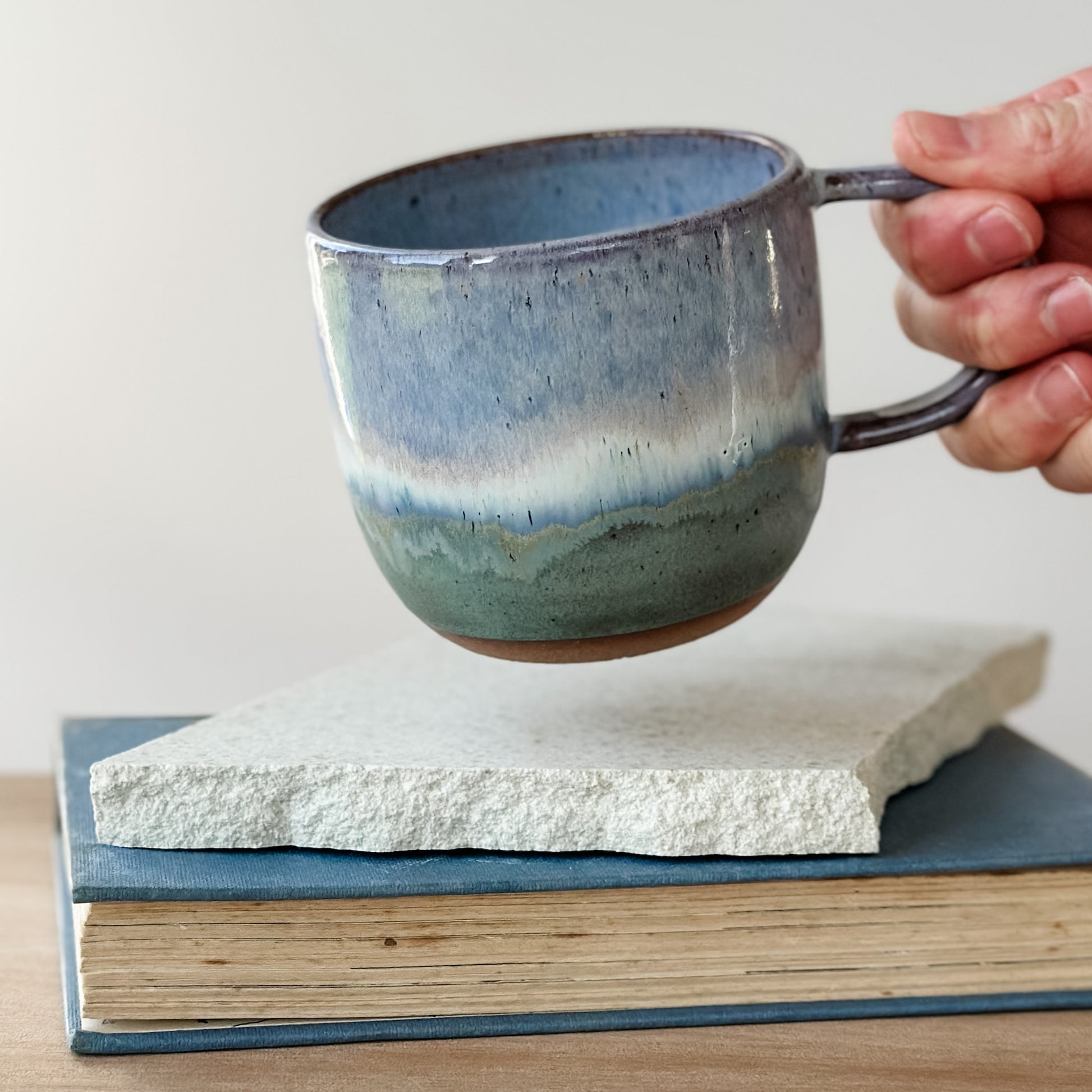 Hand holding a blue ceramic mug over a textured book
