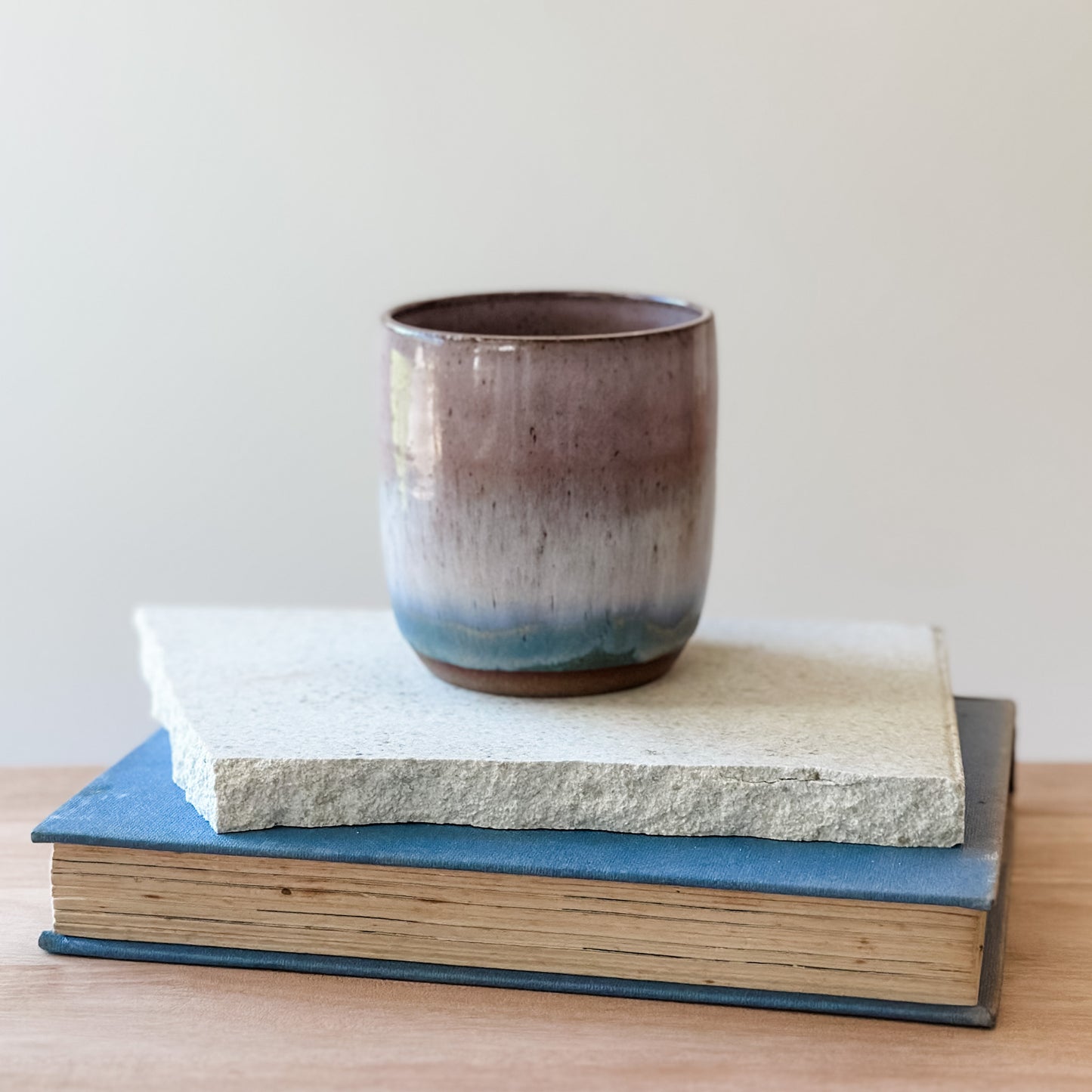 Ceramic cup on top of a tile and a book with a plain background