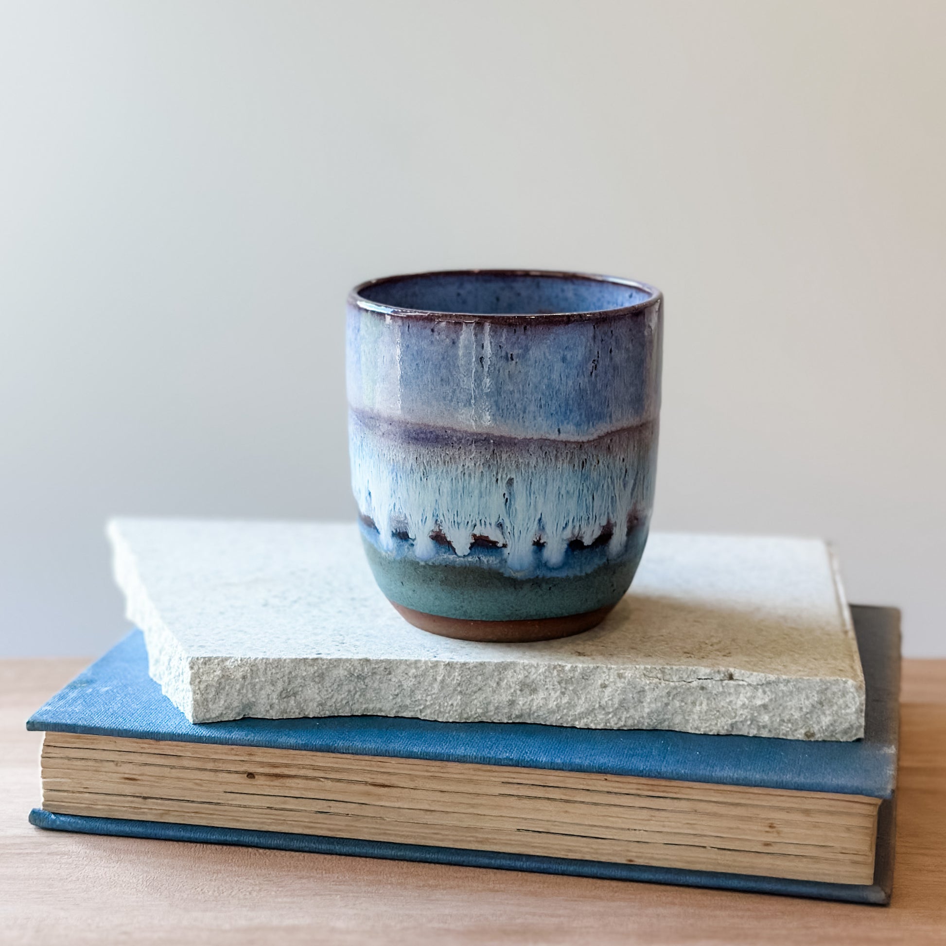 Ceramic tumbler with purple and blue glaze on top of a tile and a book