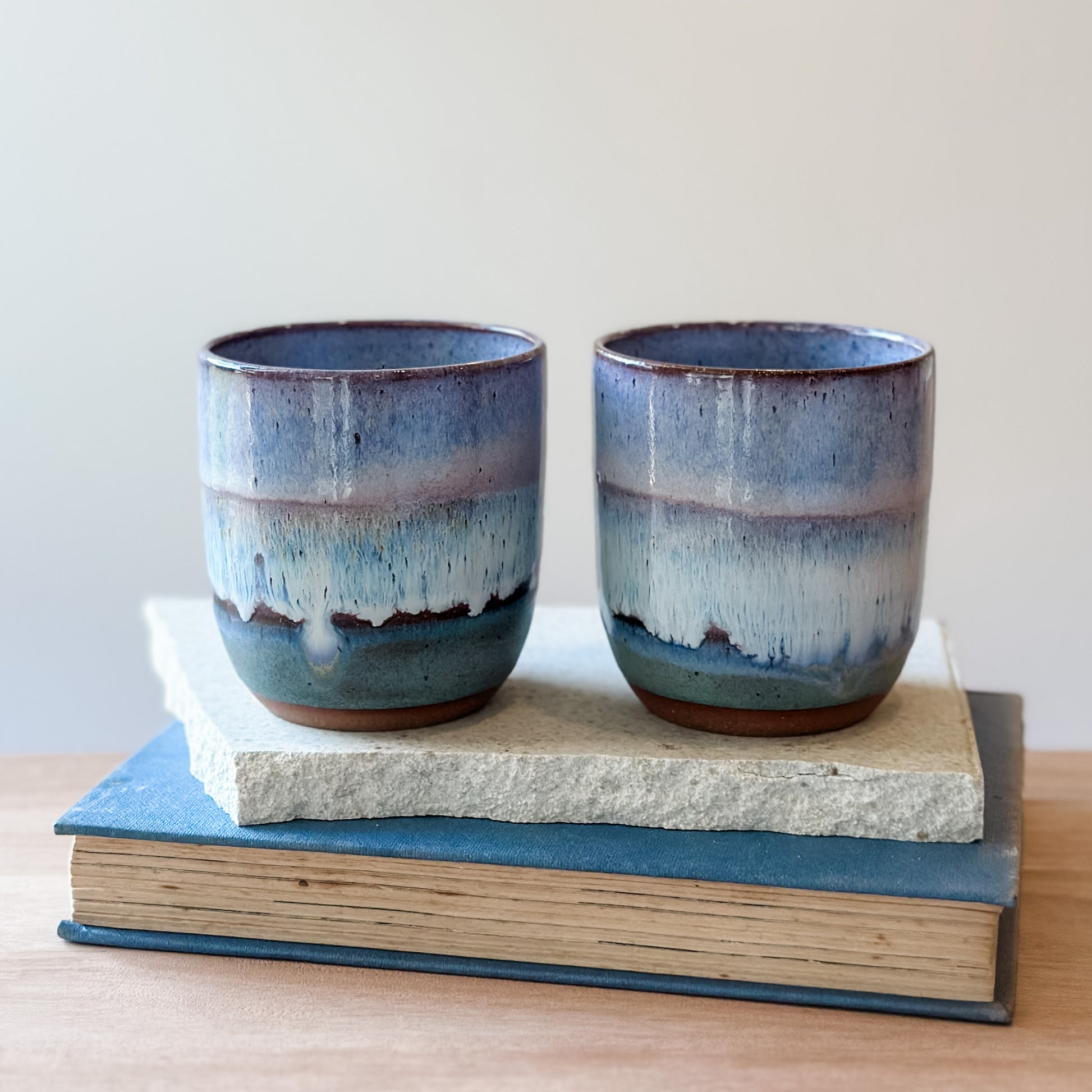 Two blue ceramic cups on a stack of tiles and books with a plain background