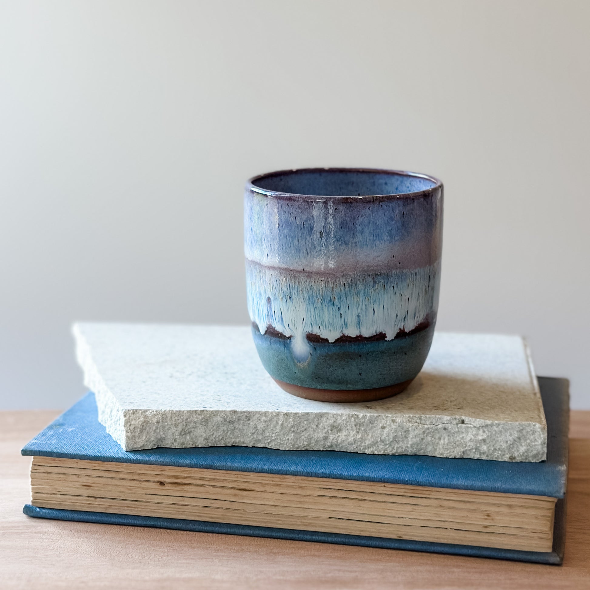 Purple and blue ceramic cup on top of a tile with a plain background