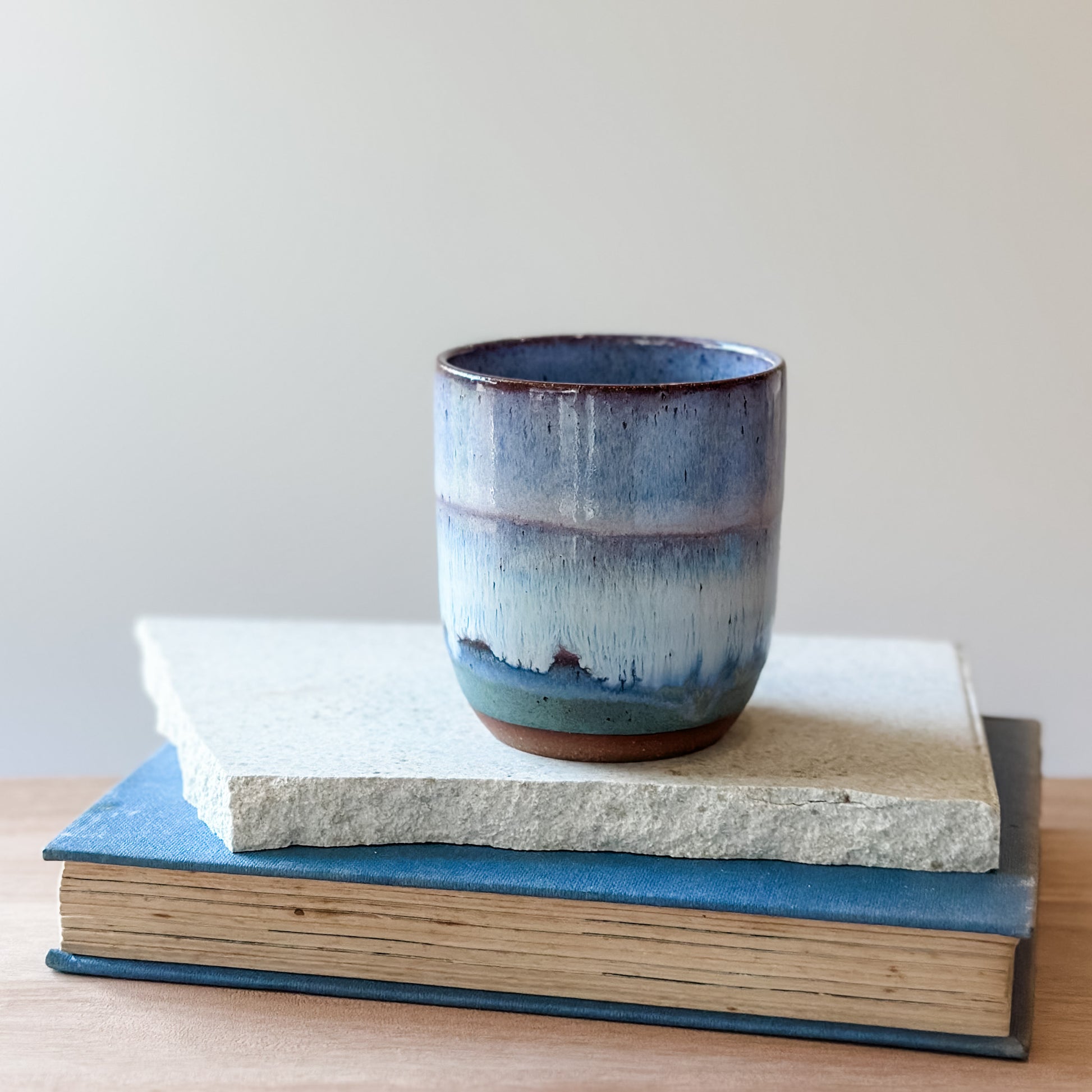 Purple and blue ceramic tumbler on a stack of books with a plain background