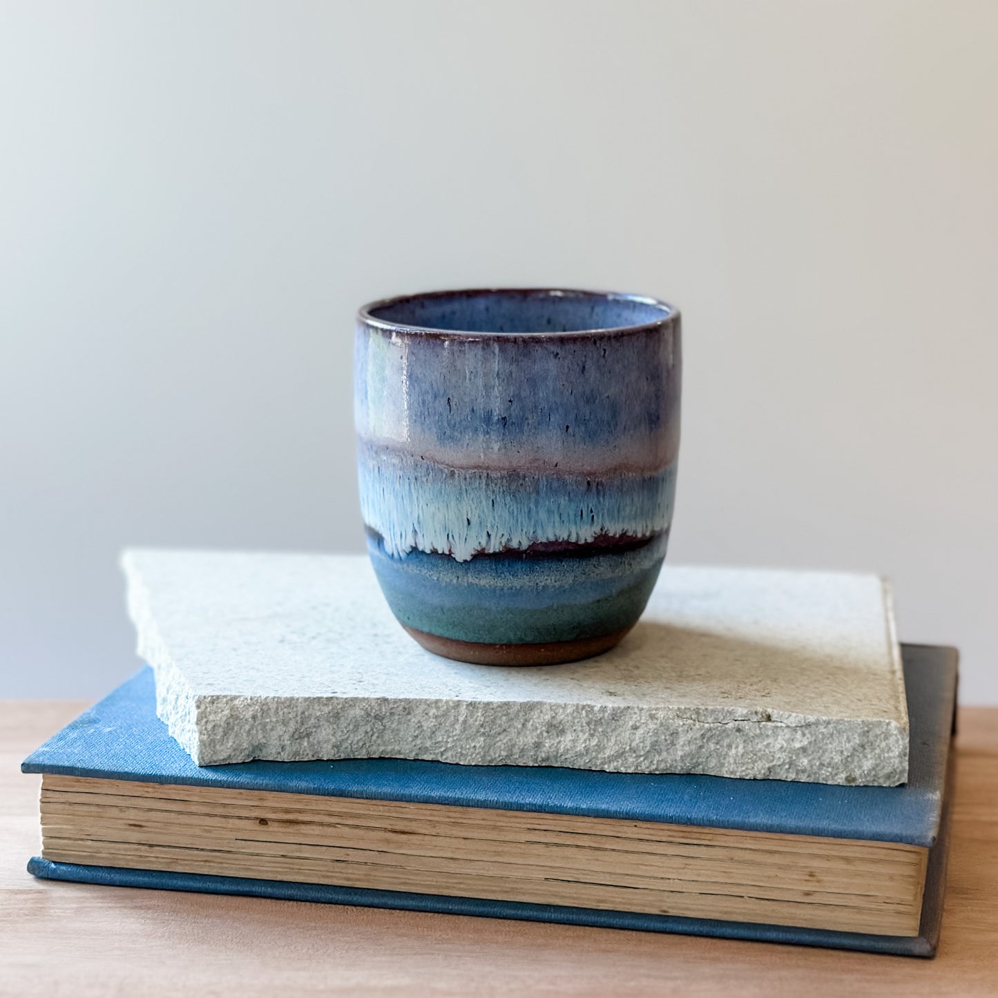 Blue ceramic cup on top of a book and a tile with a plain background