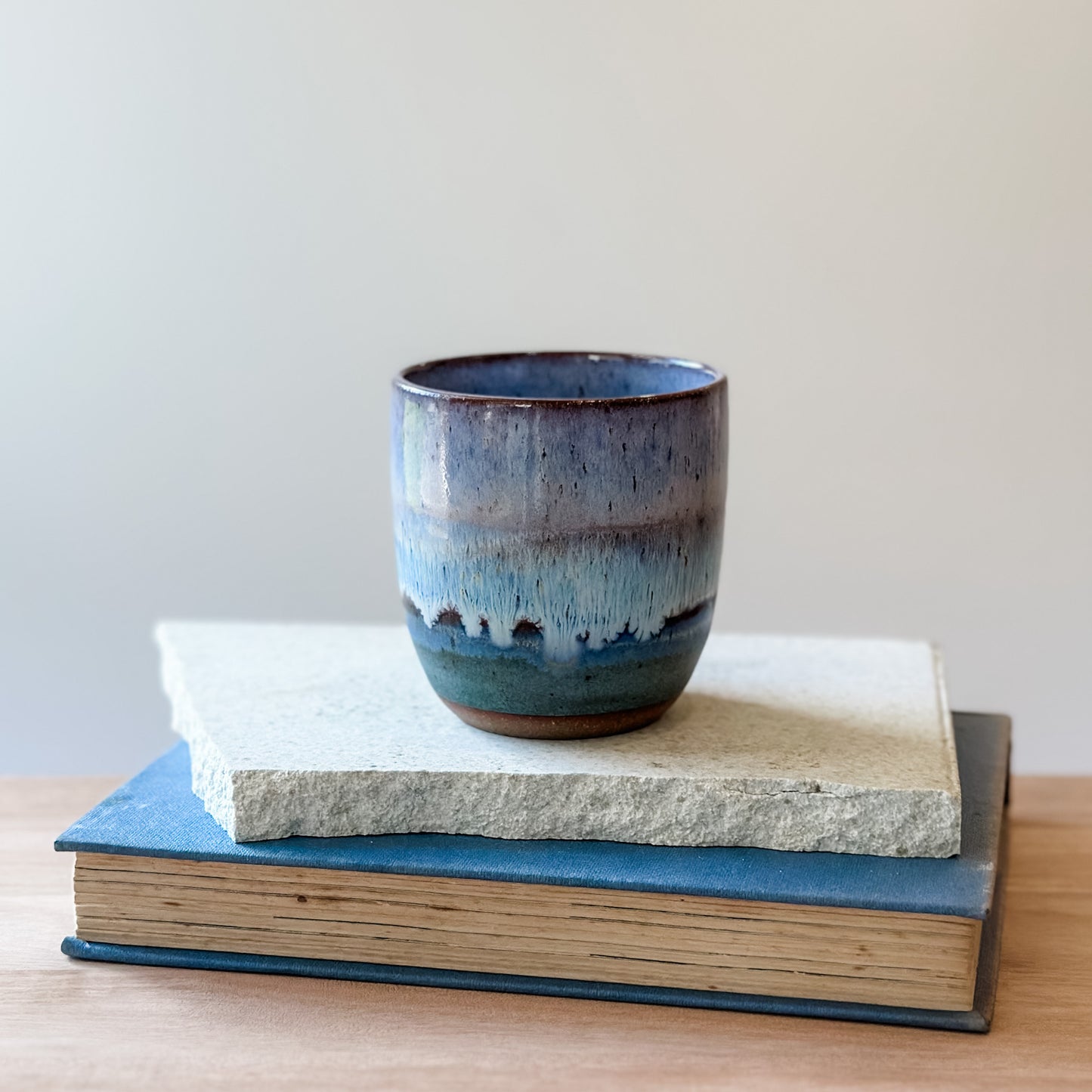 Ceramic cup with blue glaze on top of two books