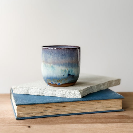 Ceramic mug with blue and purple glaze on top of a book