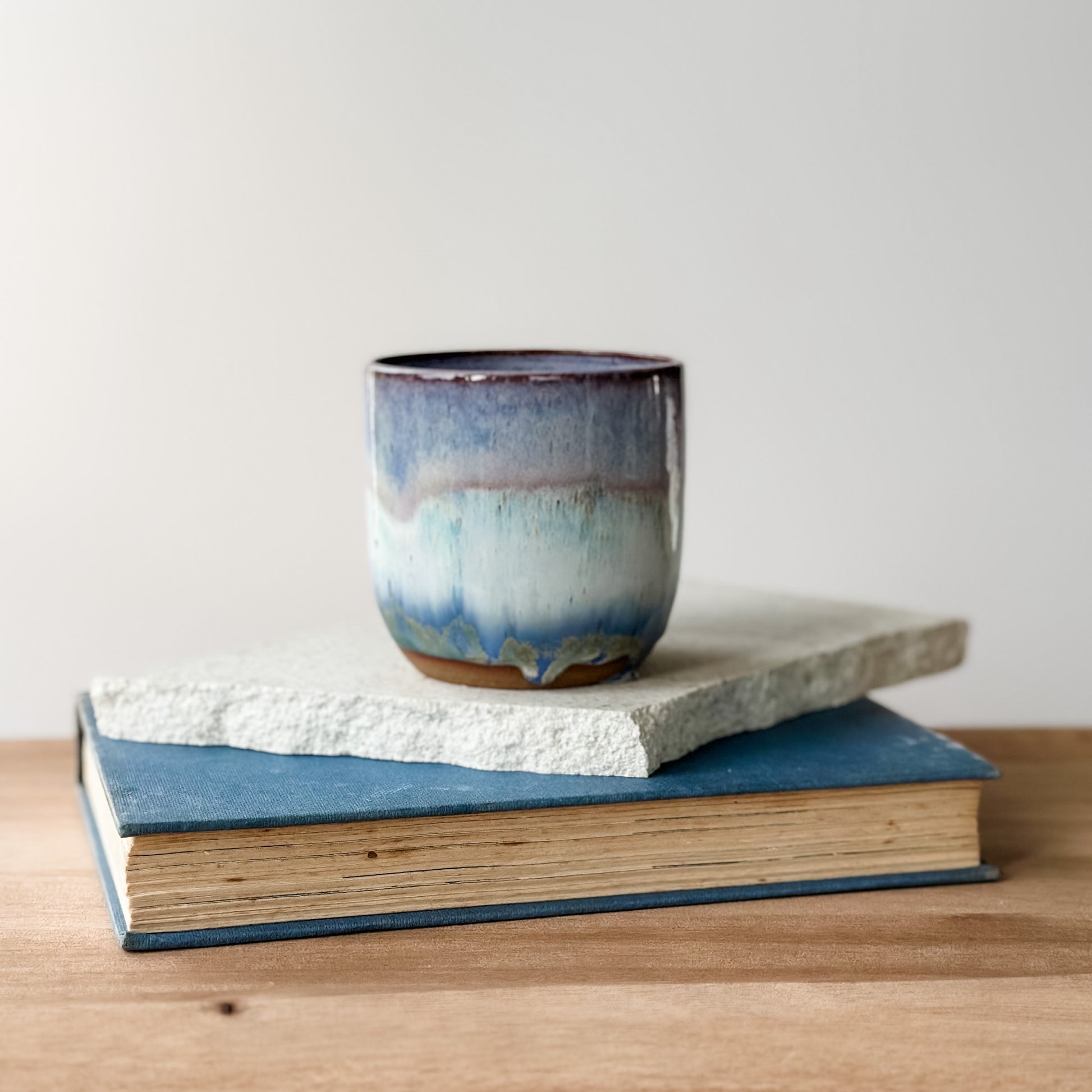 Ceramic cup with blue glaze on top of two books on a wooden surface.