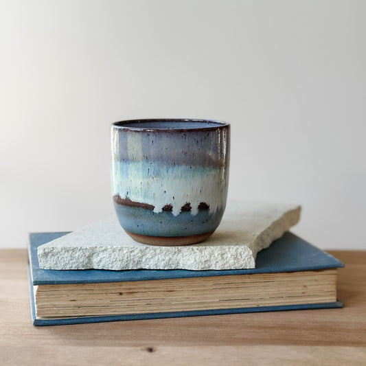 Ceramic cup with blue glaze on a stack of books against a plain background