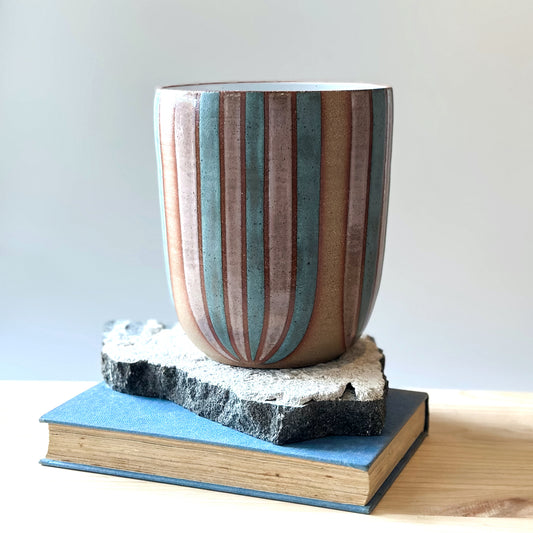 A large handmade ceramic bouquet vase sits on a tile, a book and a table. The ceramic vase is hand-painted in blush pink and denim blue glaze.