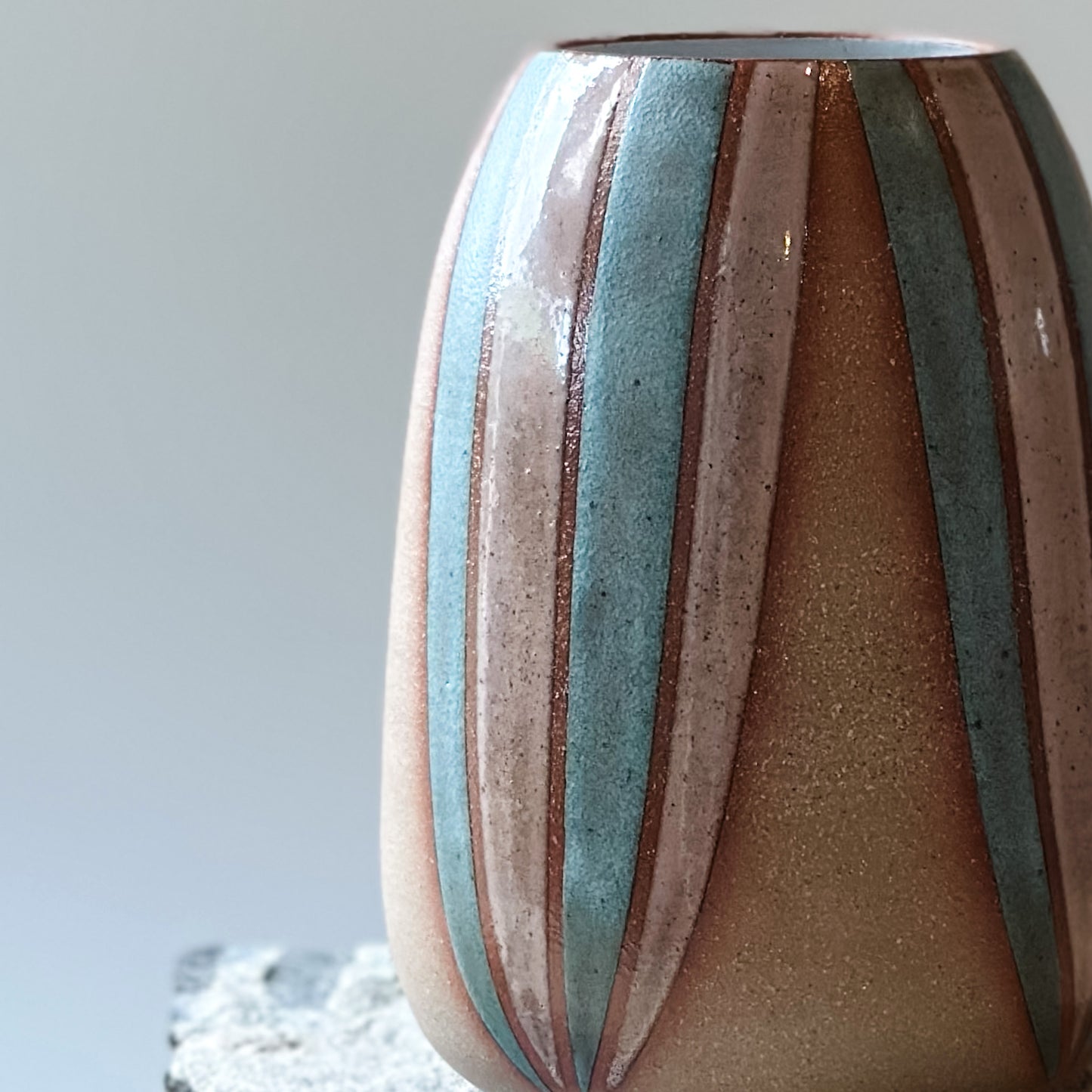A close-up view of a handmade ceramic vase, hand-painted in blush pink and blue. The bellied ceramic vase sits on a tile.