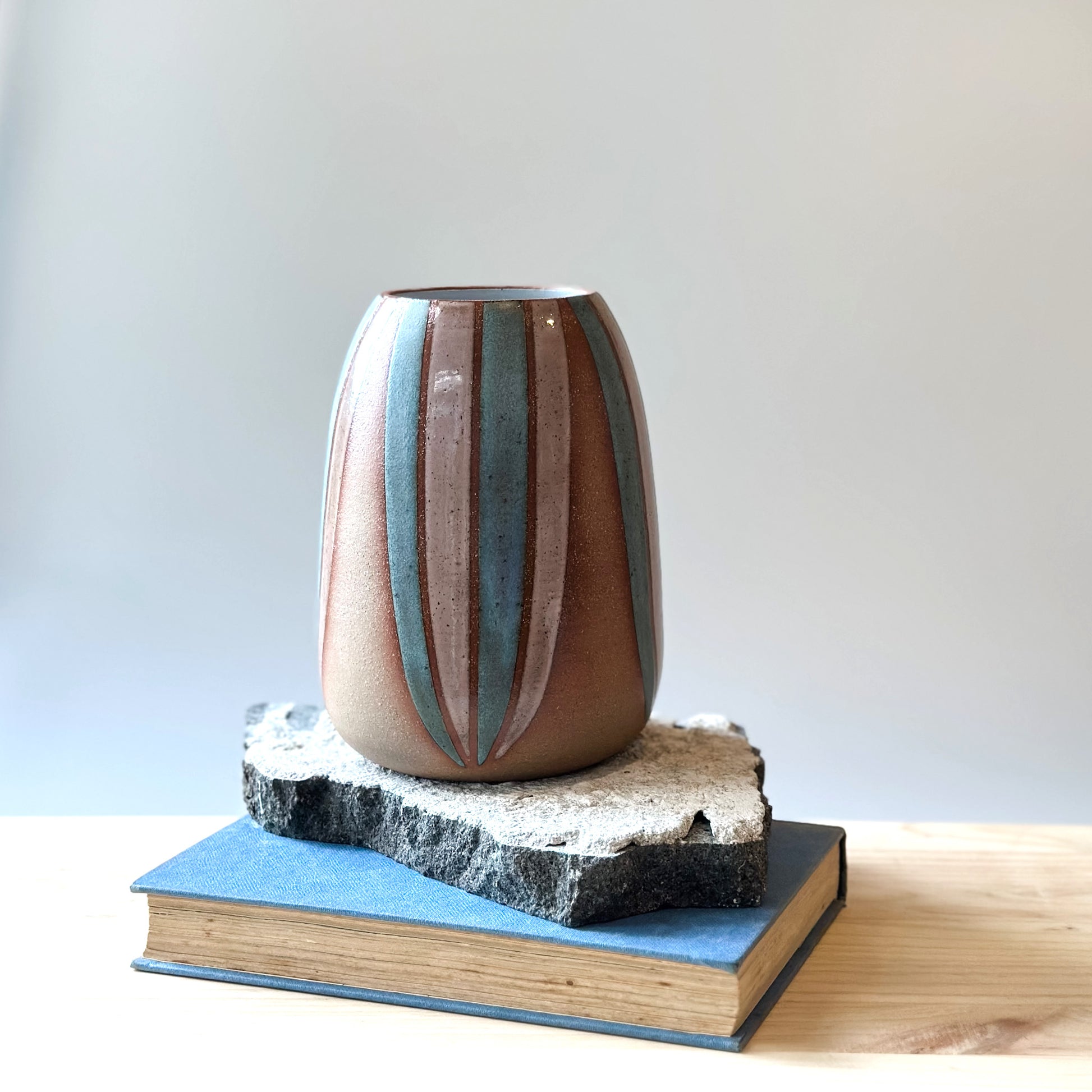 A front view of a handmade ceramic vase, hand-painted in blush pink and blue. The bellied ceramic vase is sitting on a tile on top of a table.