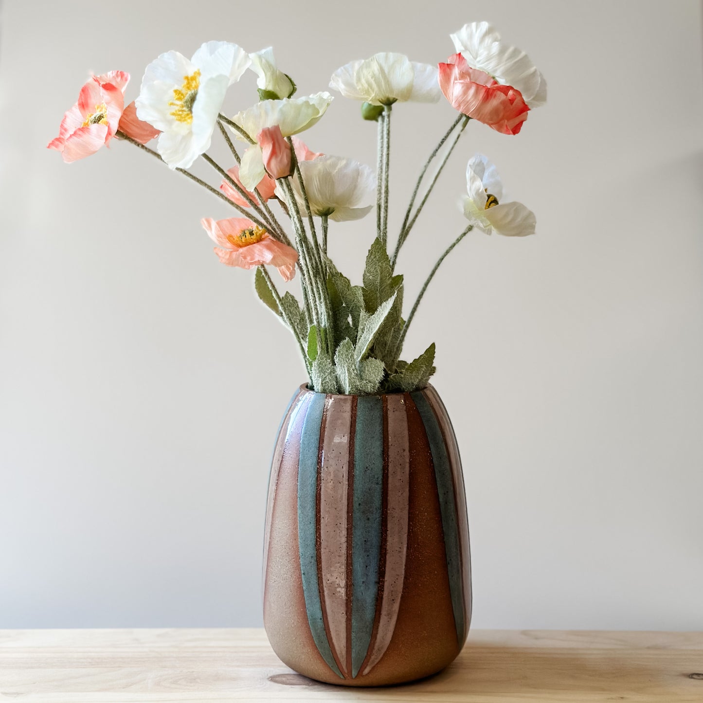 A front view of a handmade ceramic vase, hand-painted in blush pink and blue. The bellied ceramic vase sits on top of a table holding a bouquet of flowers.