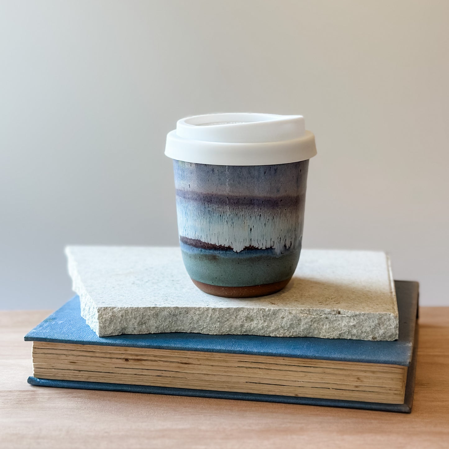 Ceramic coffee cup with a white lid on top of books with a plain background