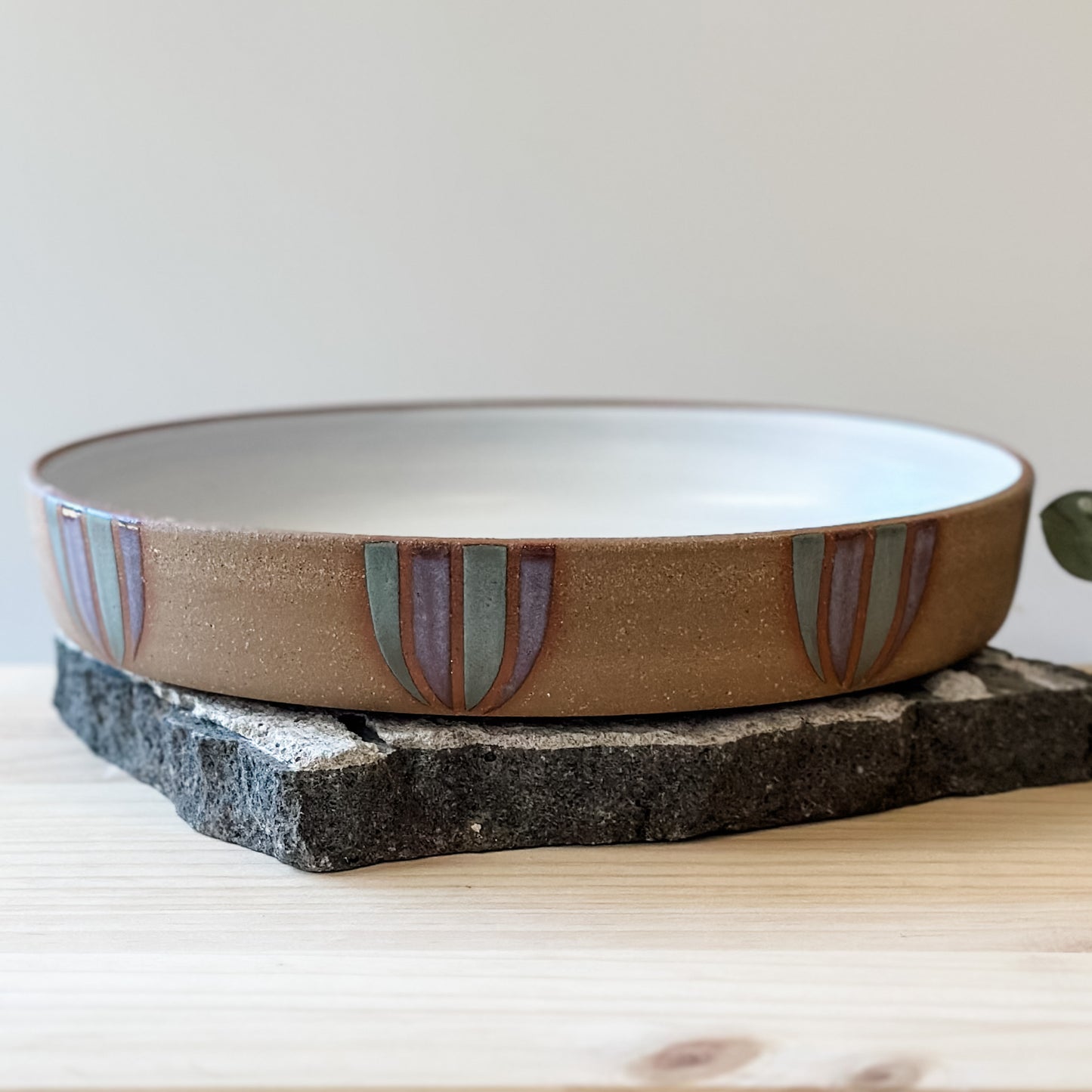 A front view of a Coastal Handmade Ceramic Platter on a tile and a wooden table. The platter has a white interior and a purple and blue-grey design on the exterior.