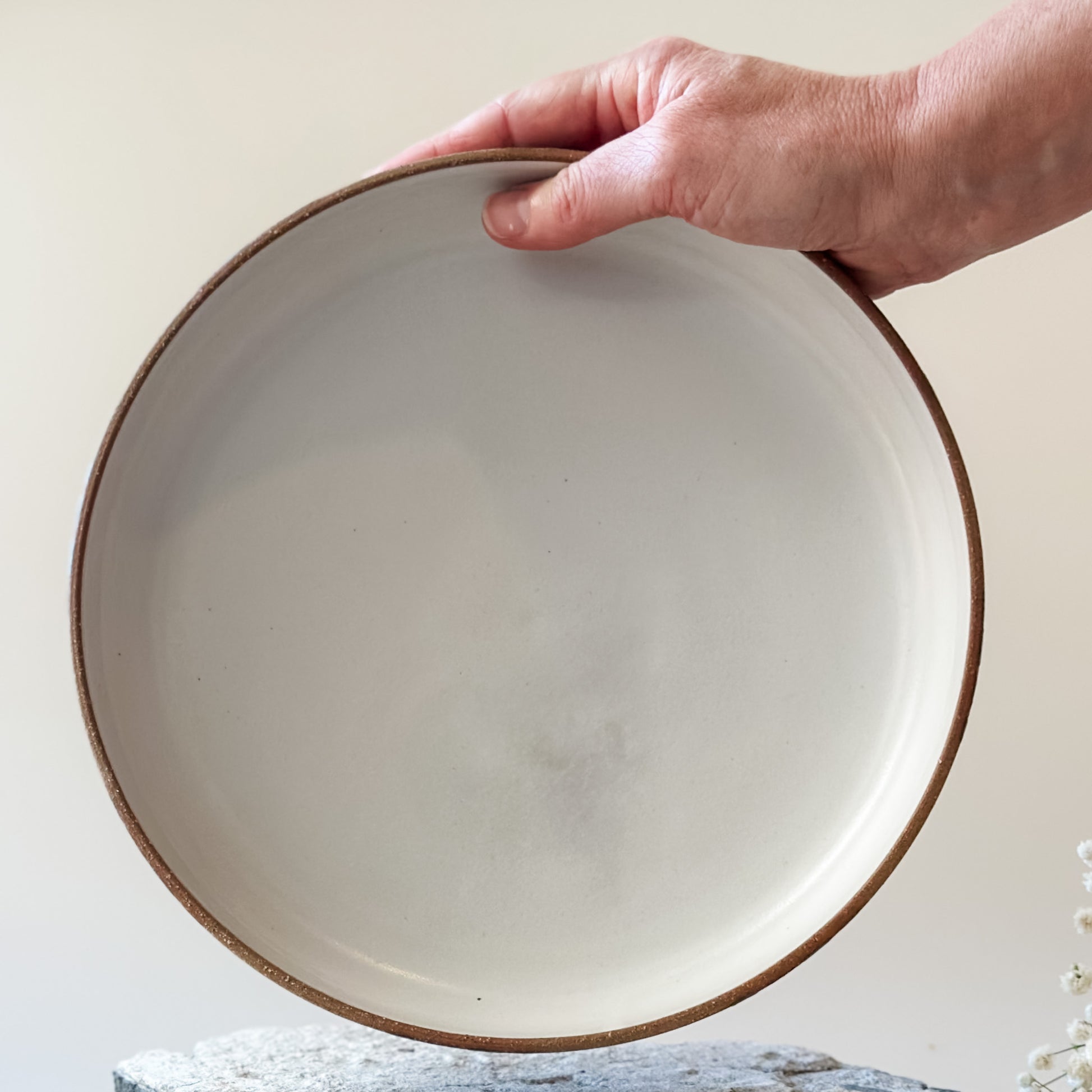 An interior view of a Coastal Handmade Ceramic Platter. The platter has a white interior. One hand is holding the platter.