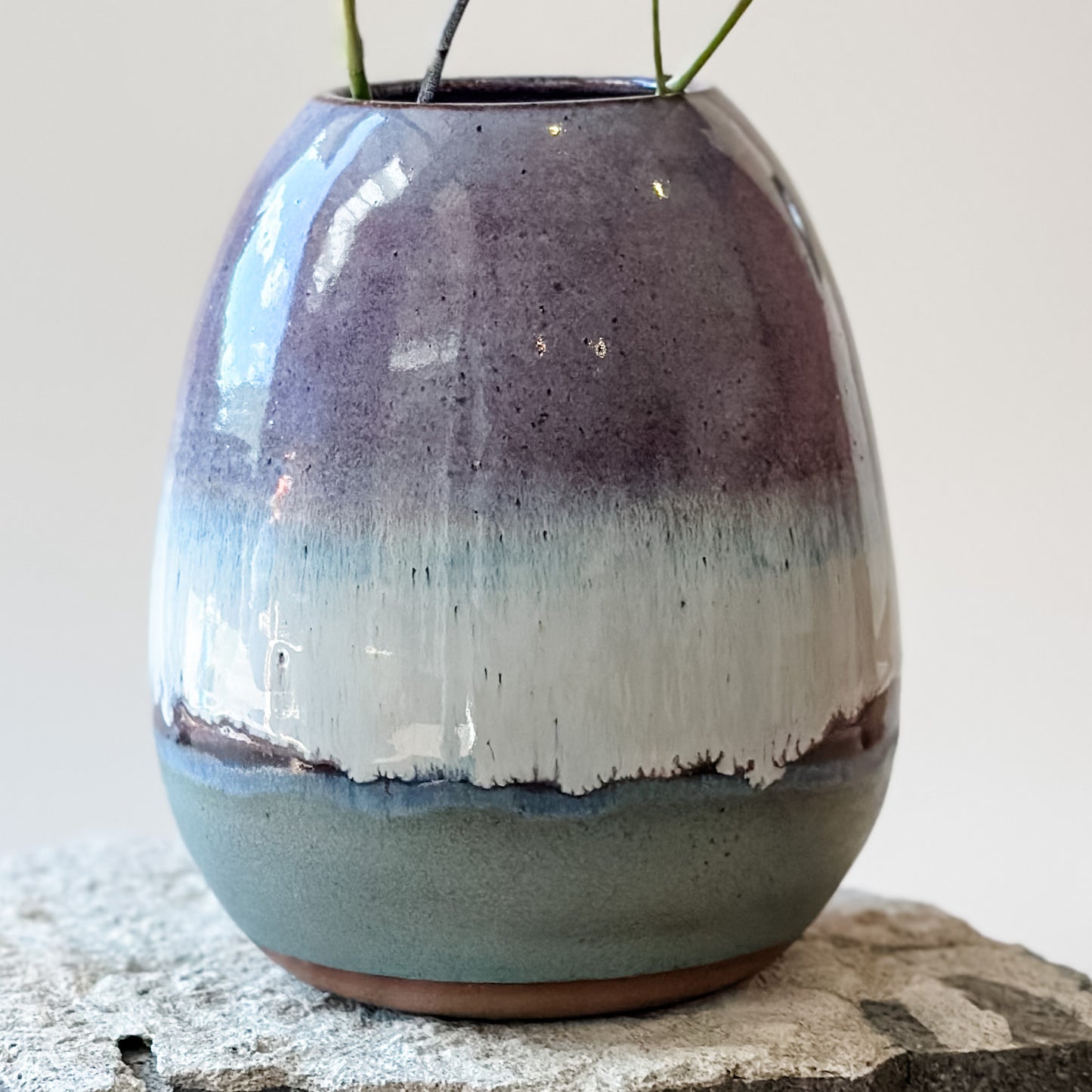 A close-up view of the Coastal Handmade Ceramic Round Vase sitting on a tile. The vase has a purple, white and blue glaze.