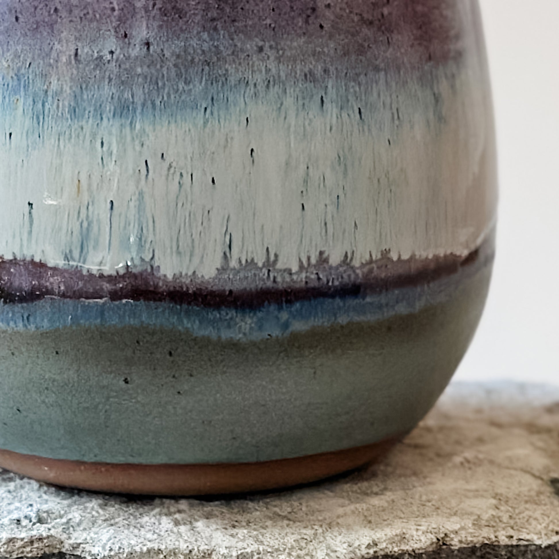 A close-up view of the glaze detail of the Coastal Handmade Ceramic Round Vase The vase has a purple, white and blue glaze. The glazes drip and melt together.