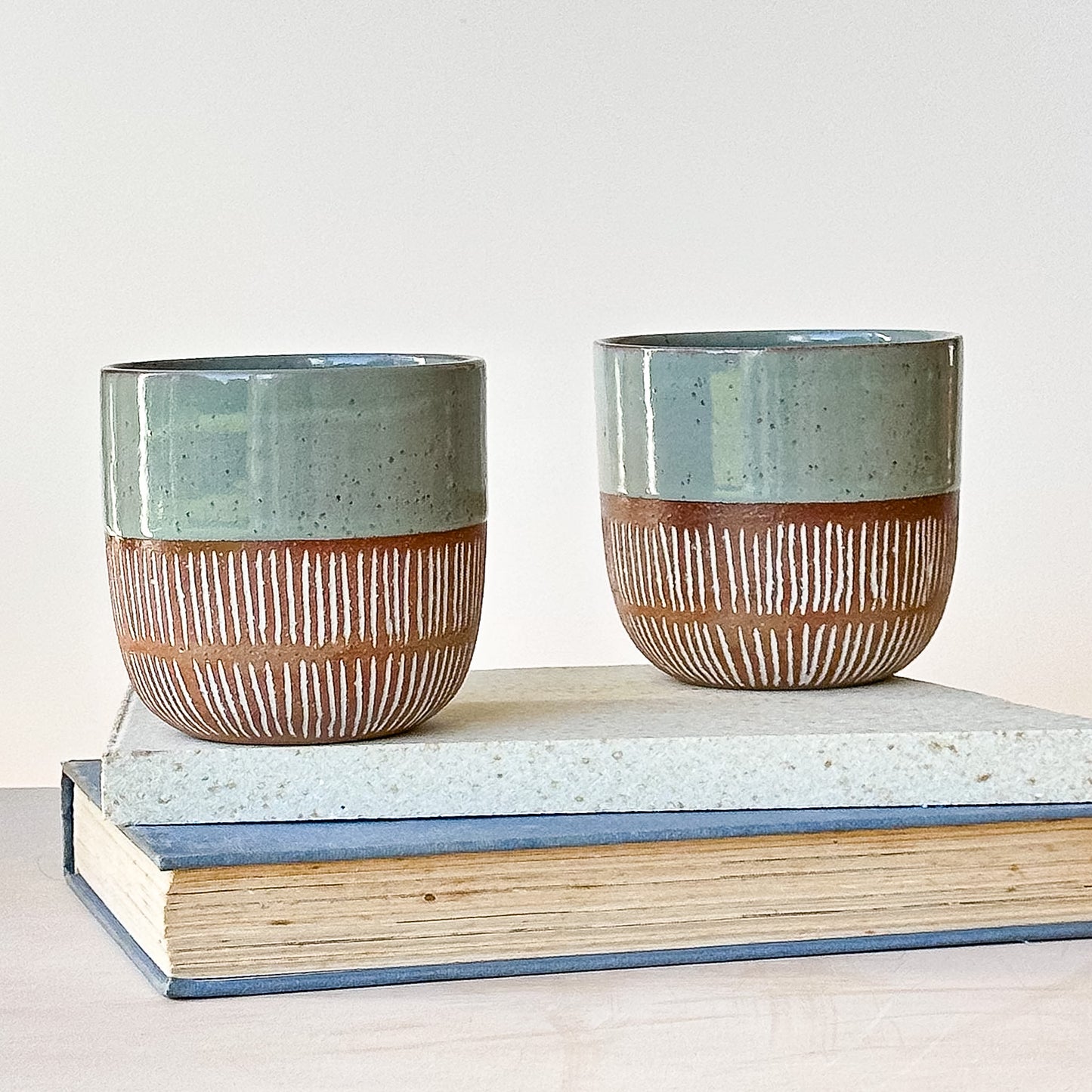 Two ceramic pots with striped design on a stack of books against a light background