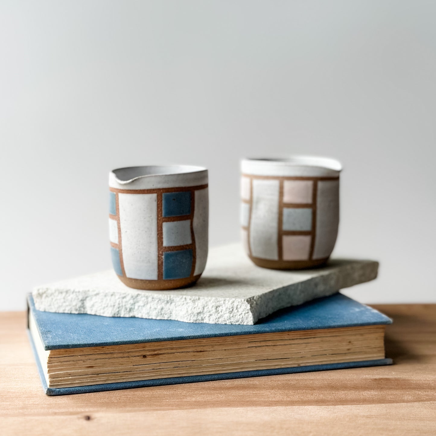 Two ceramic cups with geometric patterns on a stack of books against a light background
