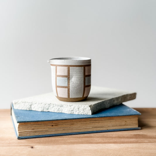 A creamer jug with a geometric pattern in pink and white glaze.