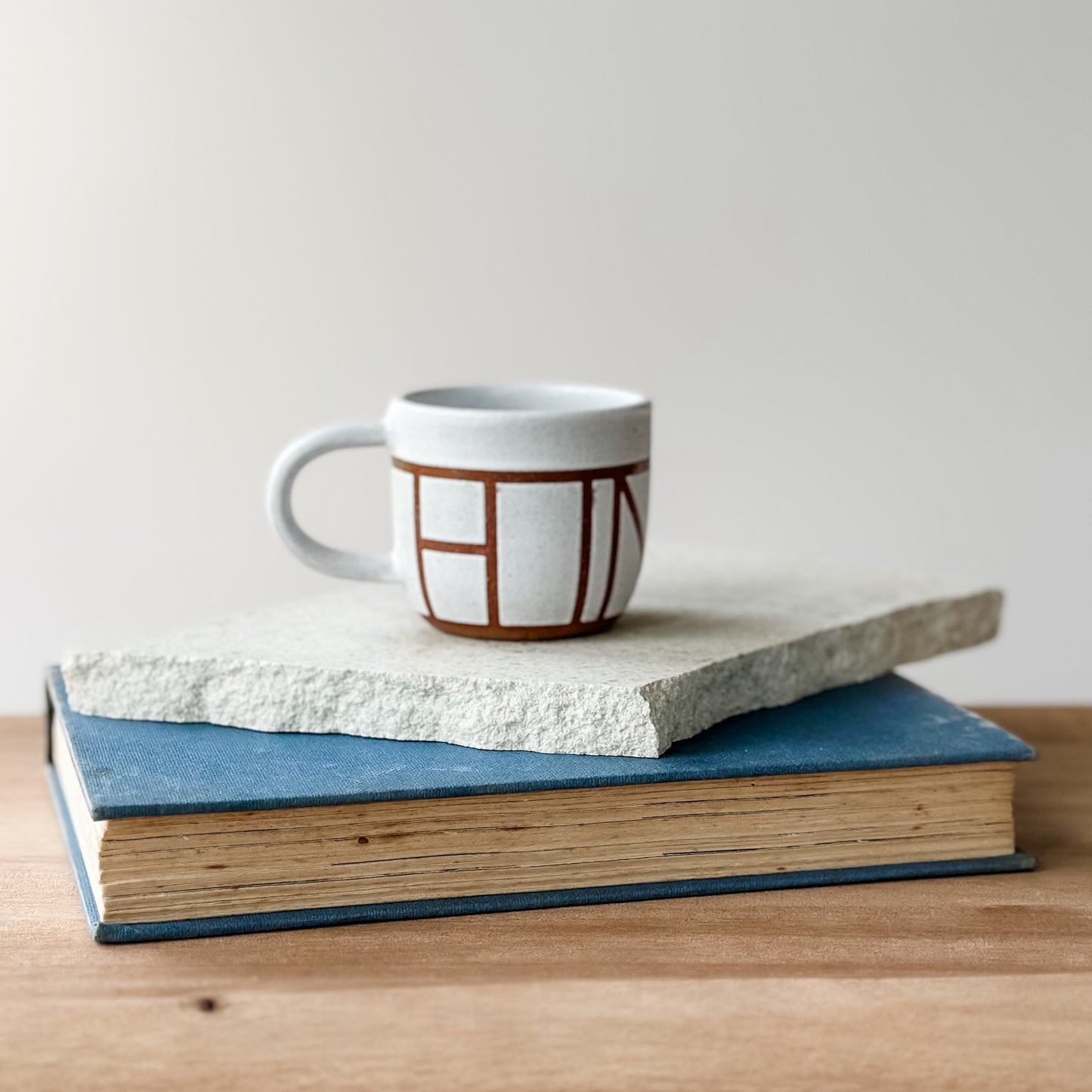 Ceramic mug with geometric design on top of two books on a wooden surface.