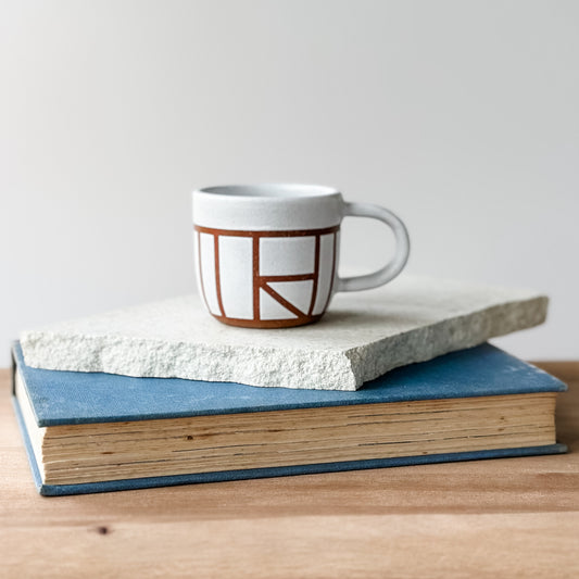 Ceramic mug with geometric design on top of two stacked books on a wooden surface.