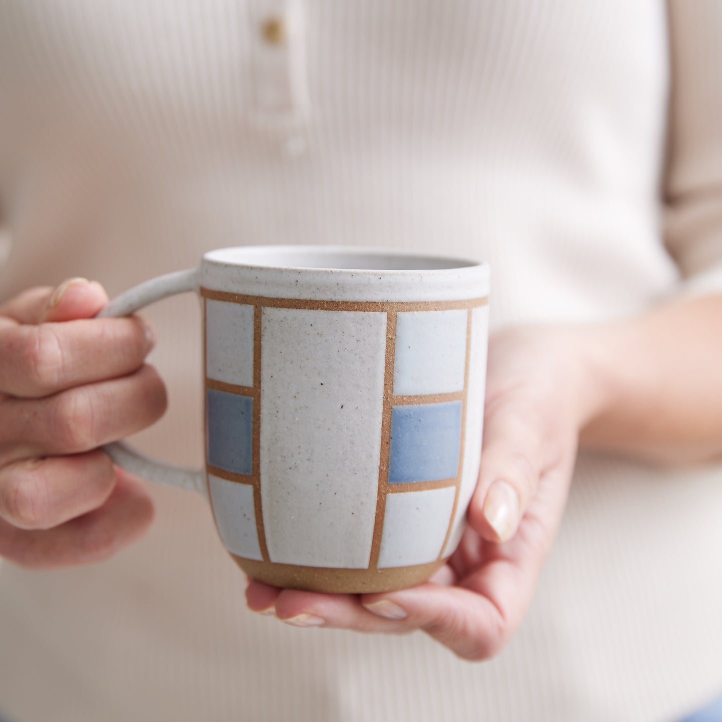 A front view of the Geometric Handmade Ceramic Mug in dark blue, white and grey glaze. The ceramic mug is held in two hands in front of a person.