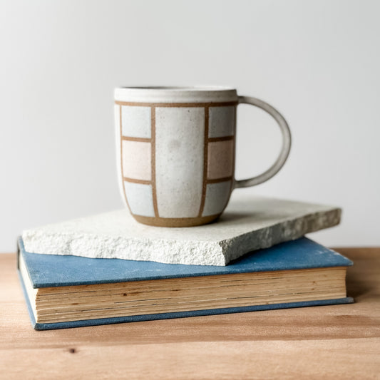 Ceramic mug with geometric pattern on top of two books on a wooden surface.