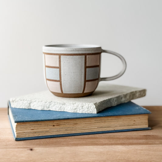 Ceramic mug with geometric pattern on top of two books on a wooden surface.