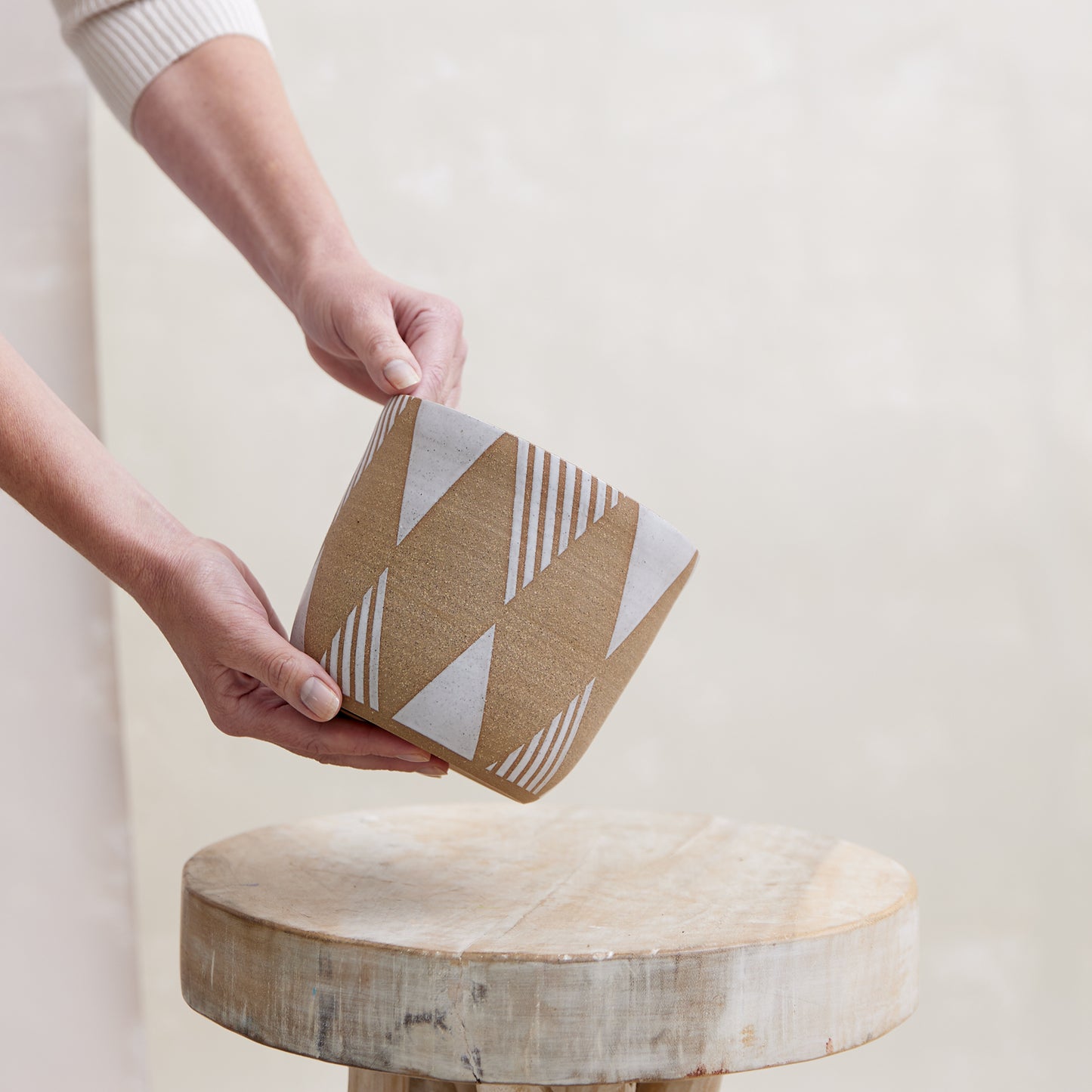 A front view of the Geometric Handmade Ceramic Planter Pot in a white glaze. The handmade planter is placed by hand atop a wooden stool in a coastal-styled setting.