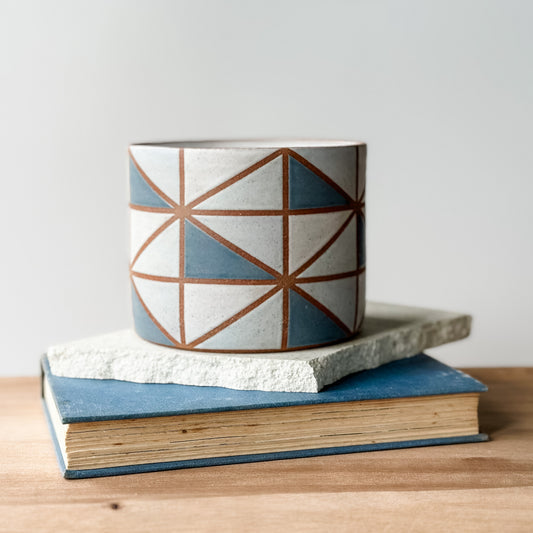 Ceramic pot with geometric design on top of a tile and a book.