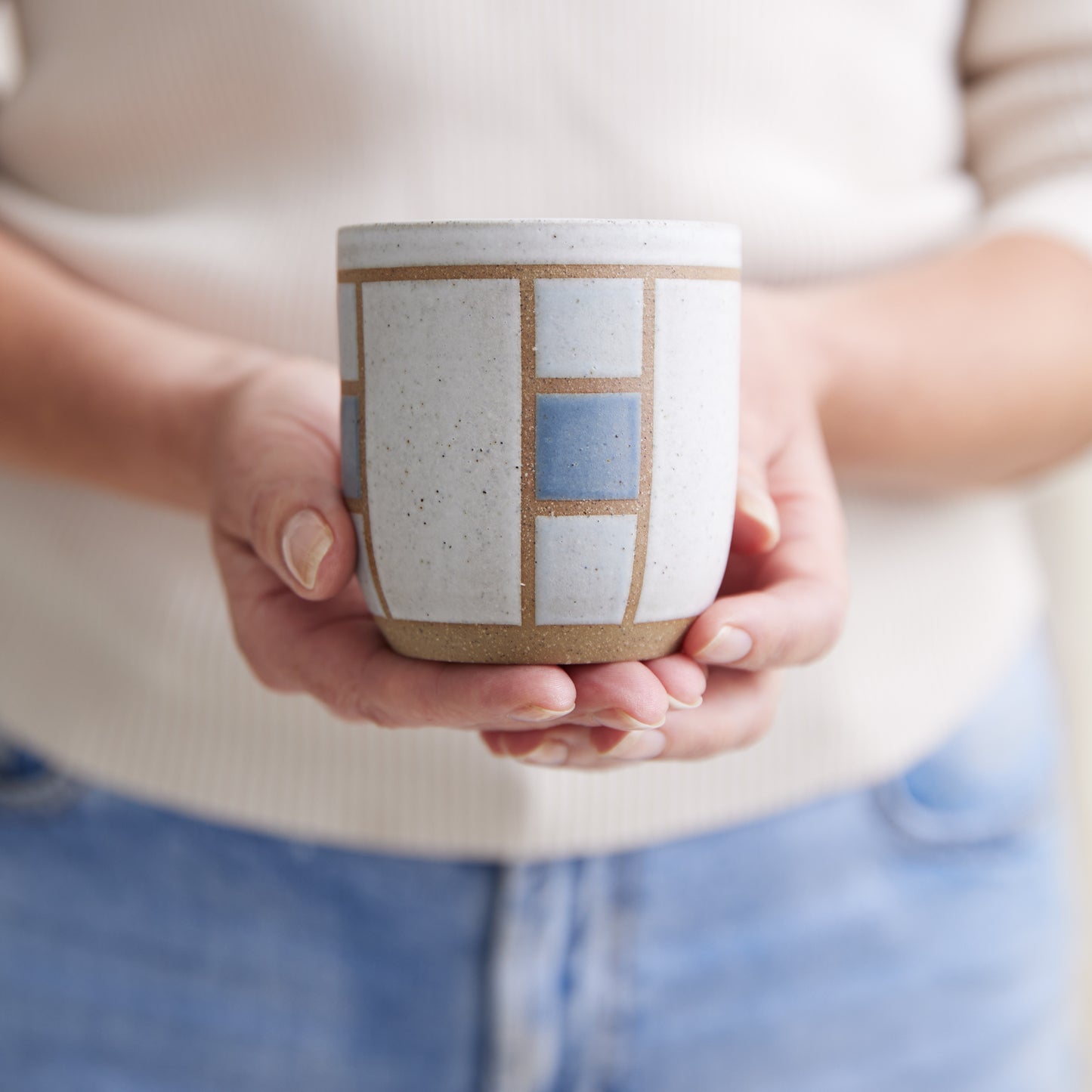 A front view of the Geometric Handmade Ceramic Tumbler in dark blue, white and grey glaze. The handmade tumbler is held in two hands.