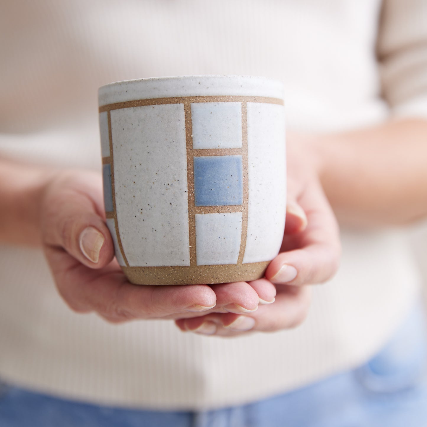 A close-up view of the Geometric Handmade Ceramic Tumbler in dark blue, white and grey glaze. The handmade tumbler is held in two hands.