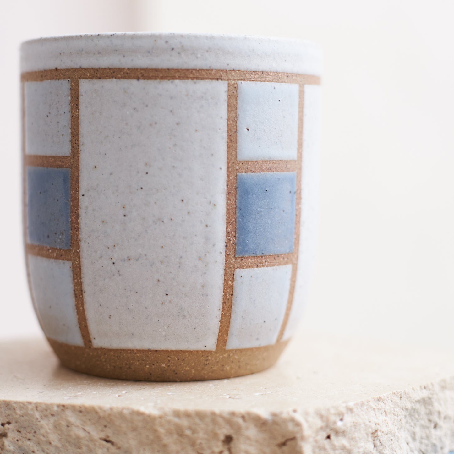 A close-up front view of the Geometric Handmade Ceramic Tumbler in dark blue, white and grey glaze. The handmade tumbler sits on a cream coloured tile.