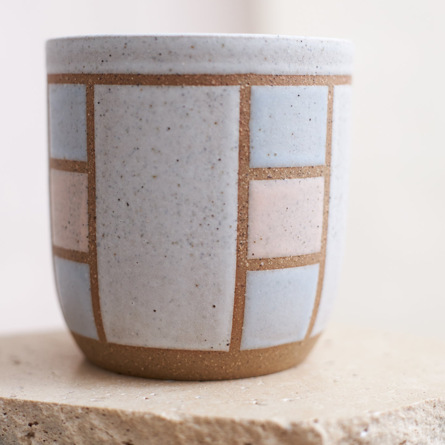 A close-up view of the 'Geometric Handmade Ceramic Tumbler' in soft pink, white and grey glaze. The handmade tumbler sits on a cream coloured tile.