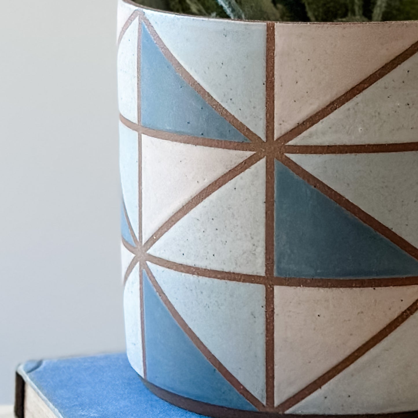 A close up view of a geometric handmade ceramic planter pot. The planter pot is painted with dark blue, pink, grey and white glaze.