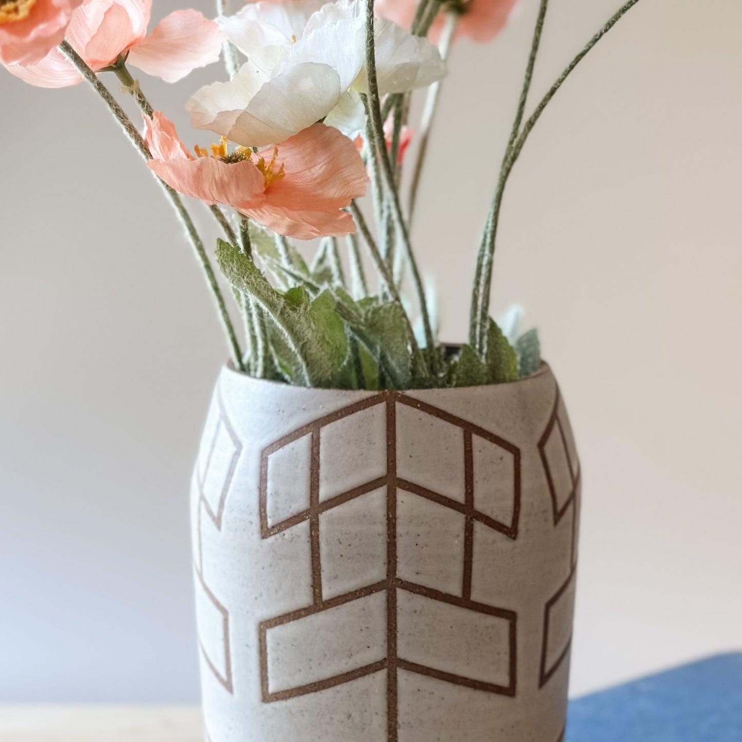 A close up view of the Geometric Handmade Ceramic vase. The Geometric Ceramic Vase is glazed white. The pattern is made by the unglazed clay. The vase holds a bunch of poppies.