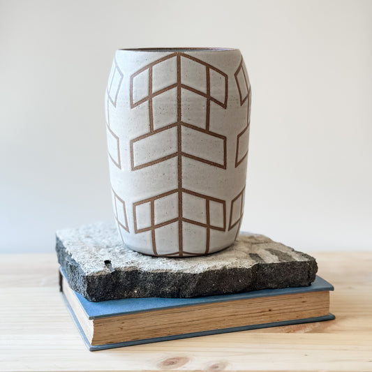 A Geometric Handmade Ceramic vase sits on a tile and on top of a table. The Geometric Ceramic Vase is glazed white. The pattern is made by the unglazed clay.
