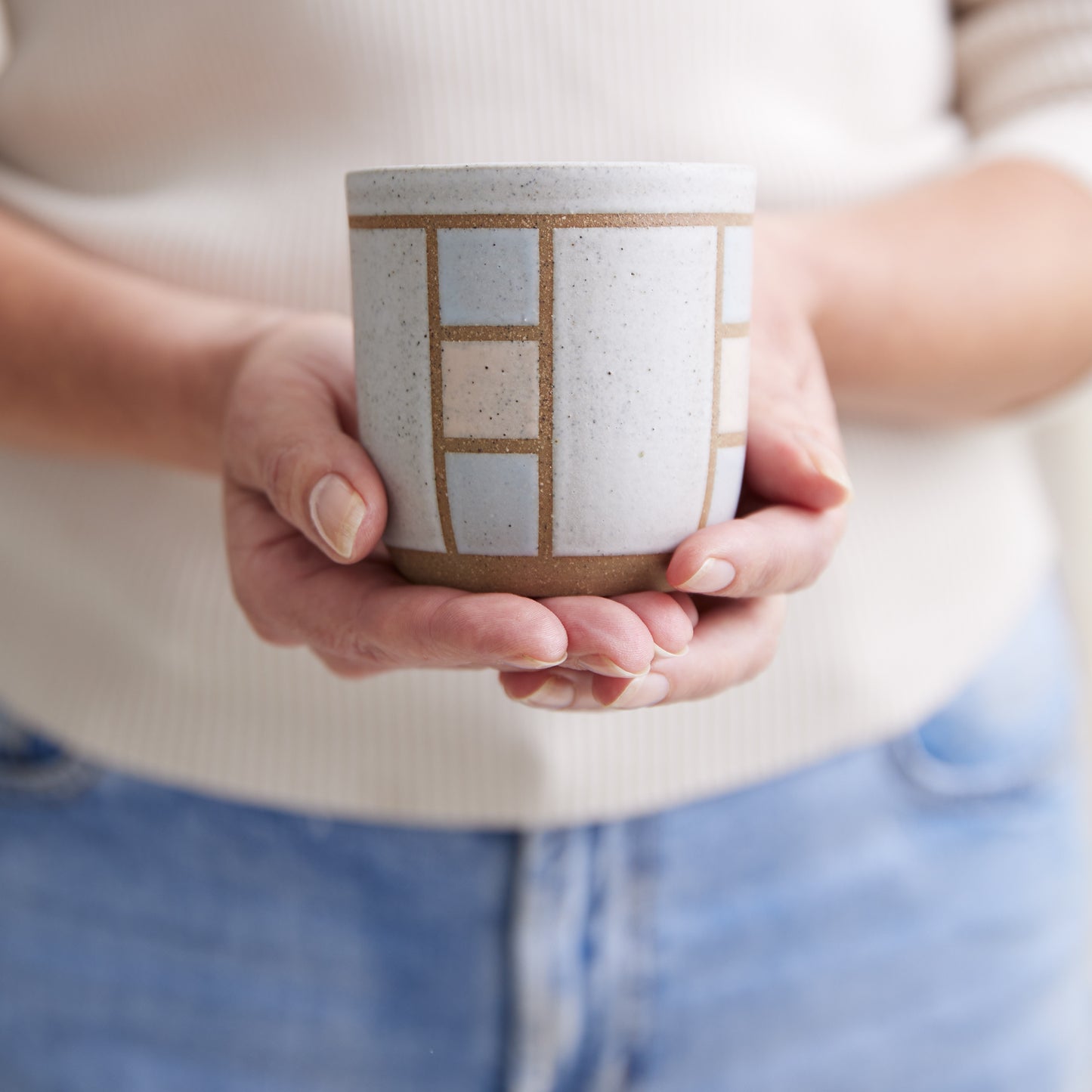 A front view of the Geometric Handmade Ceramic Tumbler in soft pink, white and grey glaze. The handmade tumbler is held by two hands.