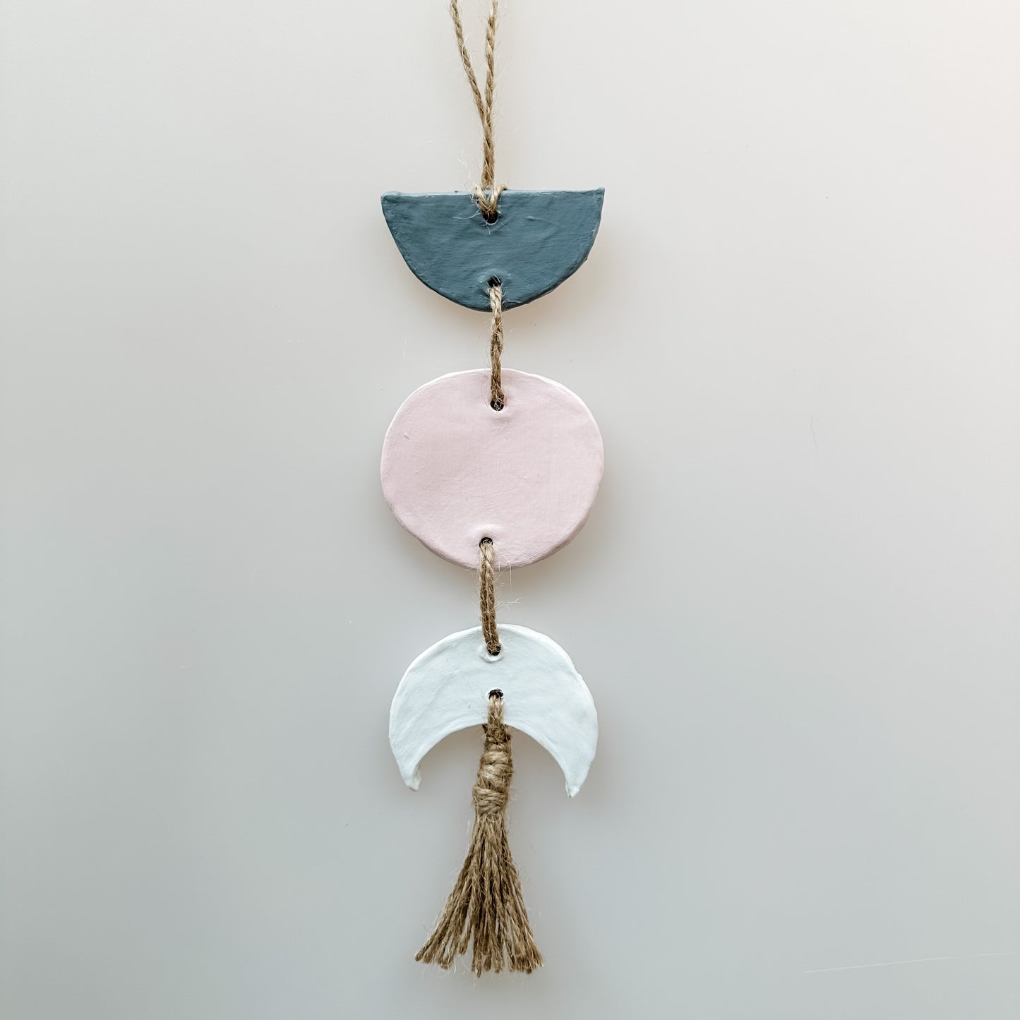 Decorative hanging with ceramic half-moon shapes and tassel on a light gray background