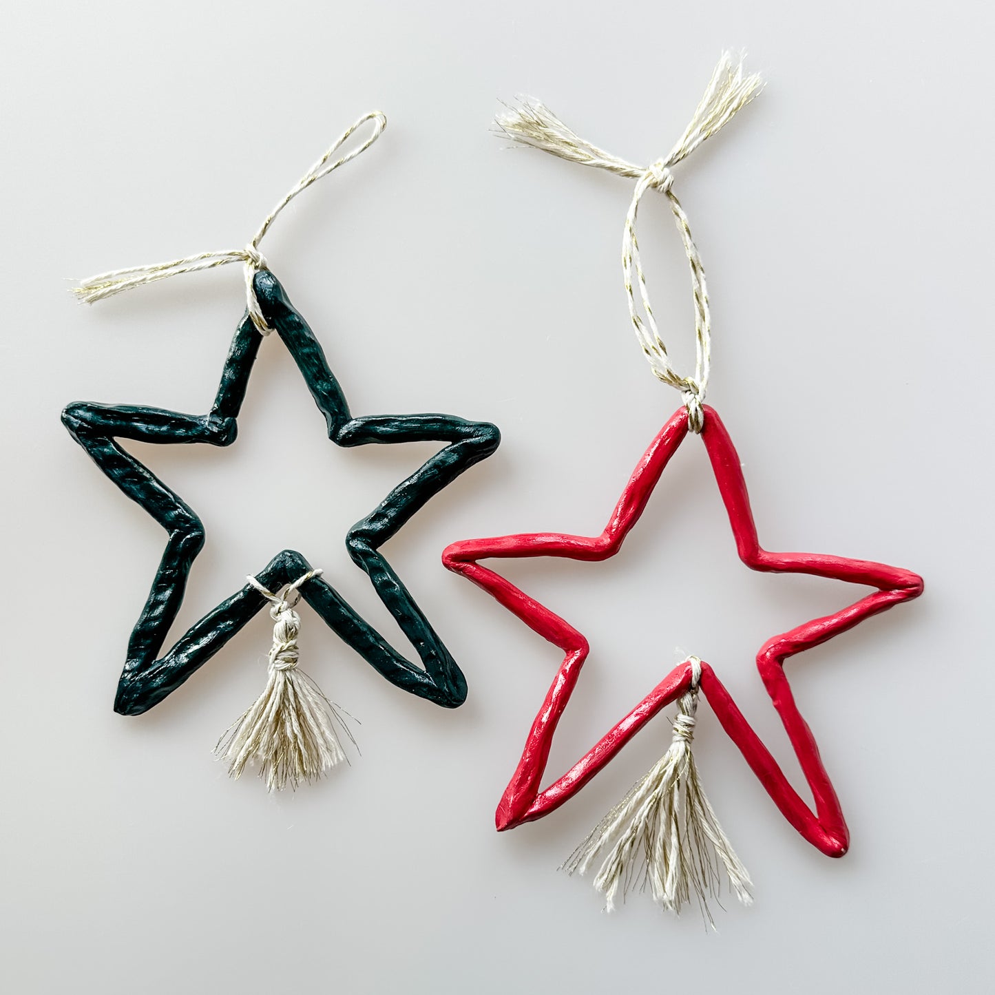 Two star-shaped clay decorations, one red and one green, on a light gray background.