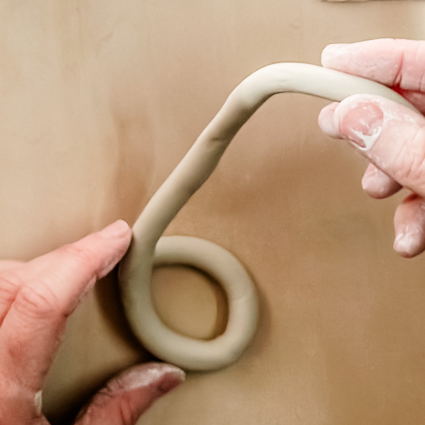 Hands shaping a piece of clay on a beige background