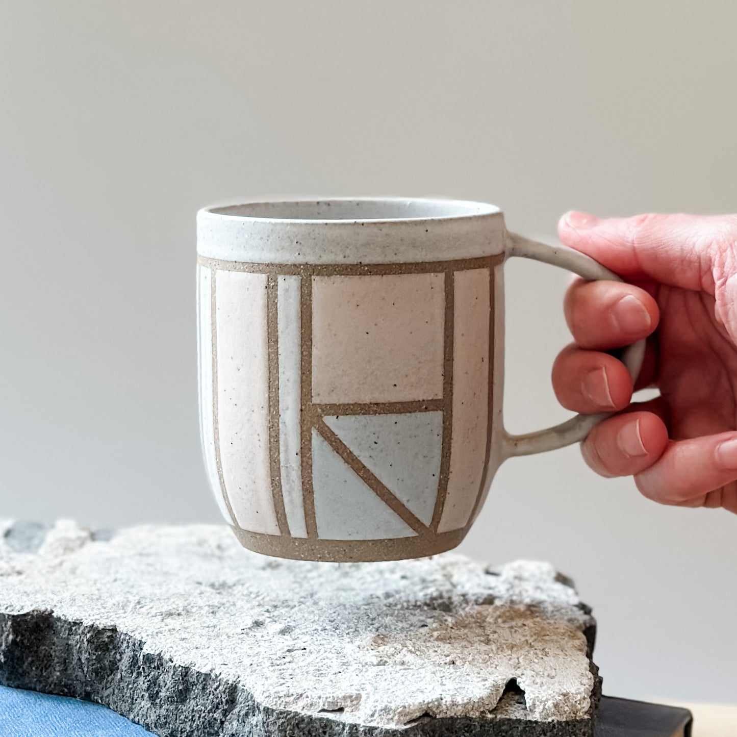 A front view of the limited edition Birdrock Ceramics geometric mug being held by a hand. The mug is painted pink, white and grey.